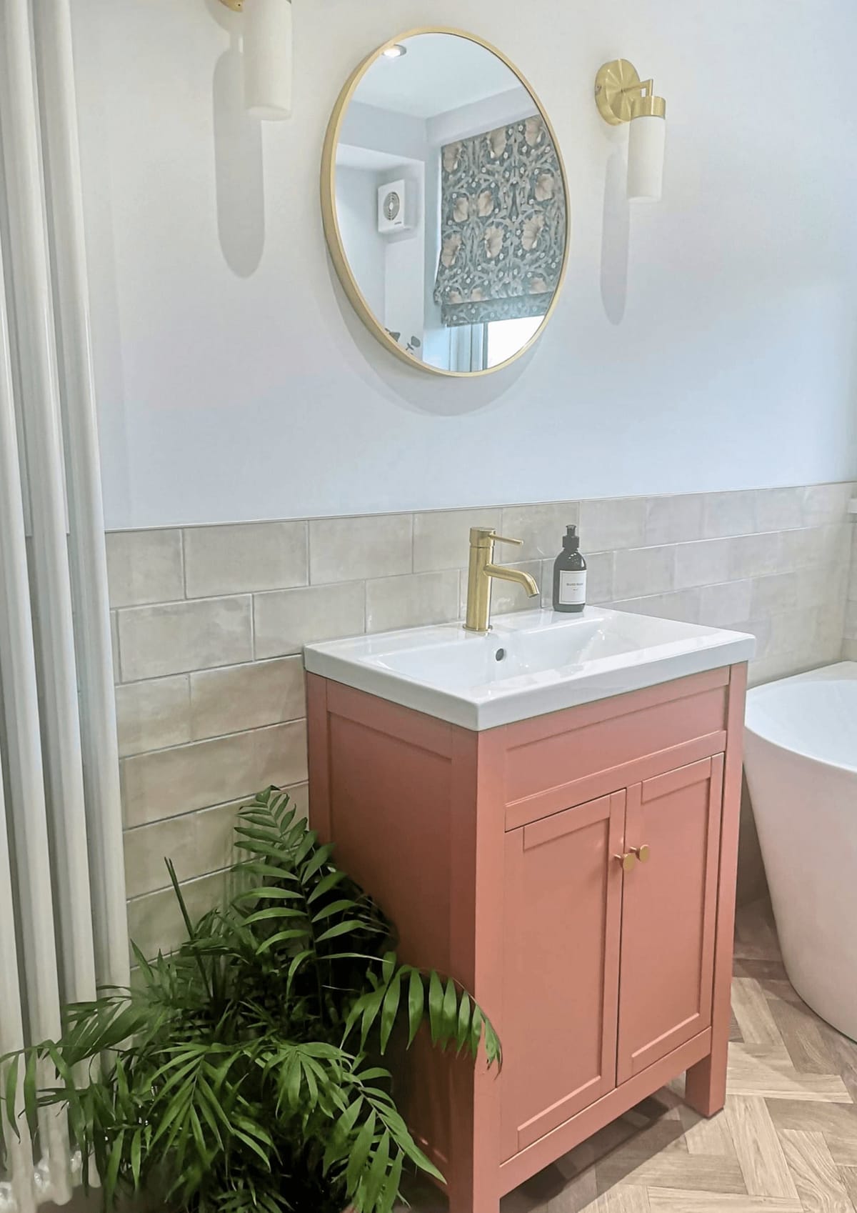 Bathroom with a pink vanity unit, round brass mirror and plants