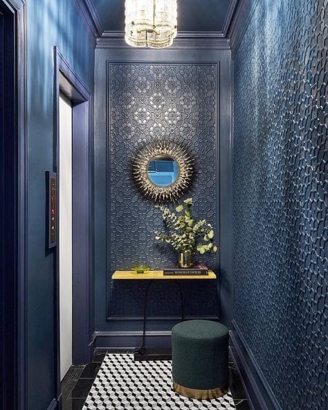 Navy hallway with patterned wallpaper, a round gold mirror and a velvet stool
