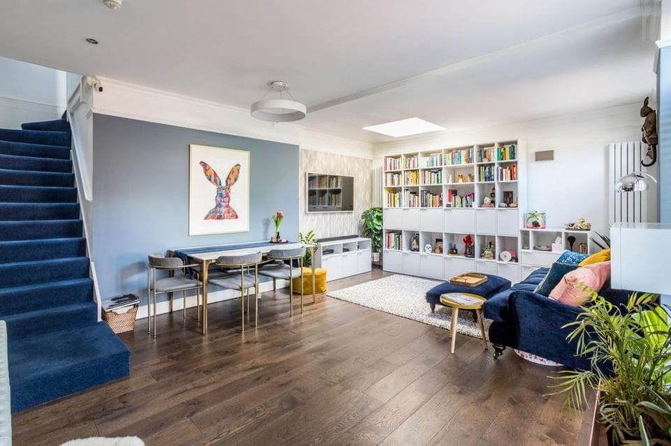 Open-plan living and dining room with blue walls, navy staircase and built-in bookshelves