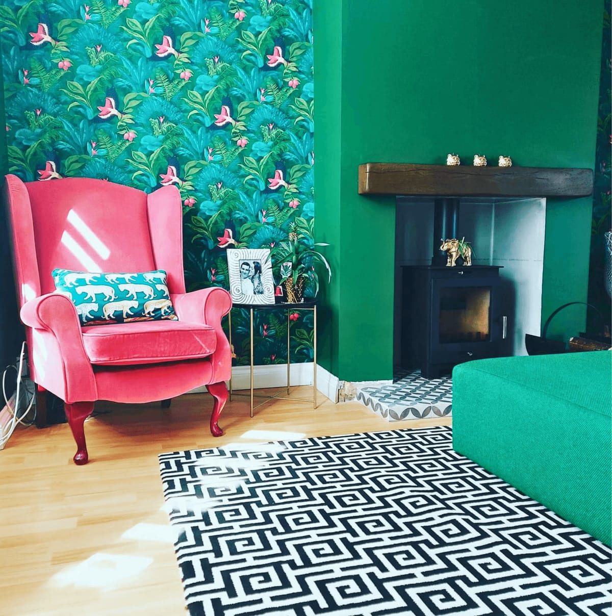 Living room with a pink wingback chair, green walls and tropical wallpaper