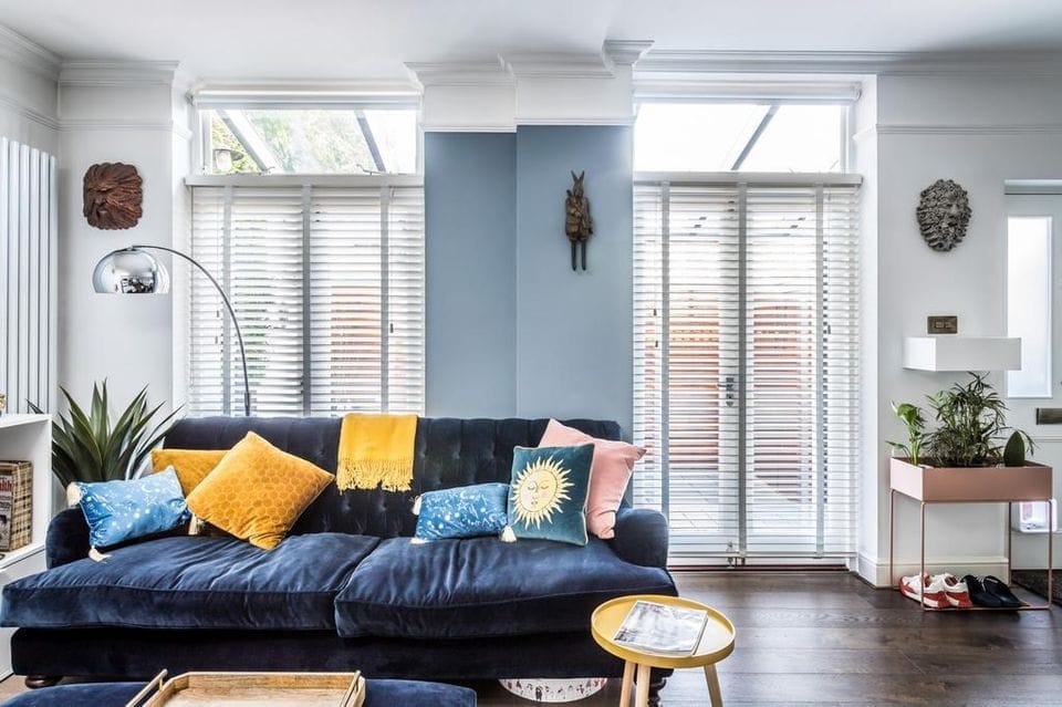 Navy velvet sofa with mustard and teal cushions under French doors